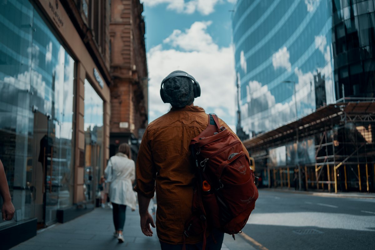 A job seeker with headphones and a backpack walking down a city street